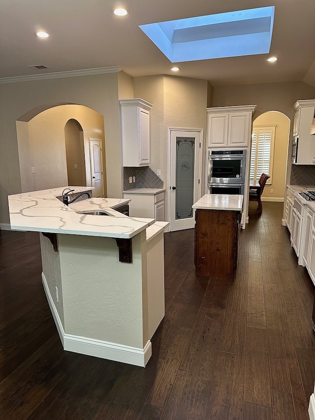 kitchen featuring a spacious island, dark wood-style floors, backsplash, and a sink