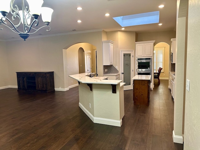 kitchen with double oven, decorative backsplash, a peninsula, arched walkways, and dark wood-style flooring