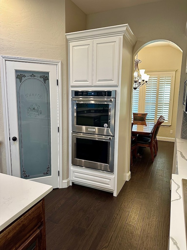 kitchen featuring dark wood finished floors, stainless steel double oven, white cabinets, and an inviting chandelier