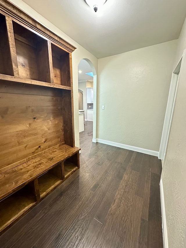 mudroom with arched walkways, dark wood finished floors, and baseboards