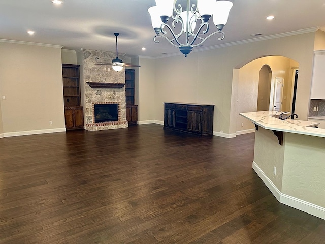 unfurnished living room with dark wood-style floors, arched walkways, crown molding, ceiling fan with notable chandelier, and a large fireplace