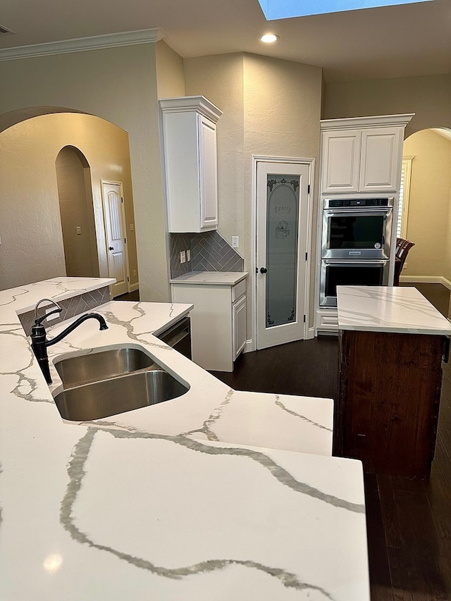 kitchen featuring stainless steel double oven, dark wood finished floors, arched walkways, a sink, and white cabinetry