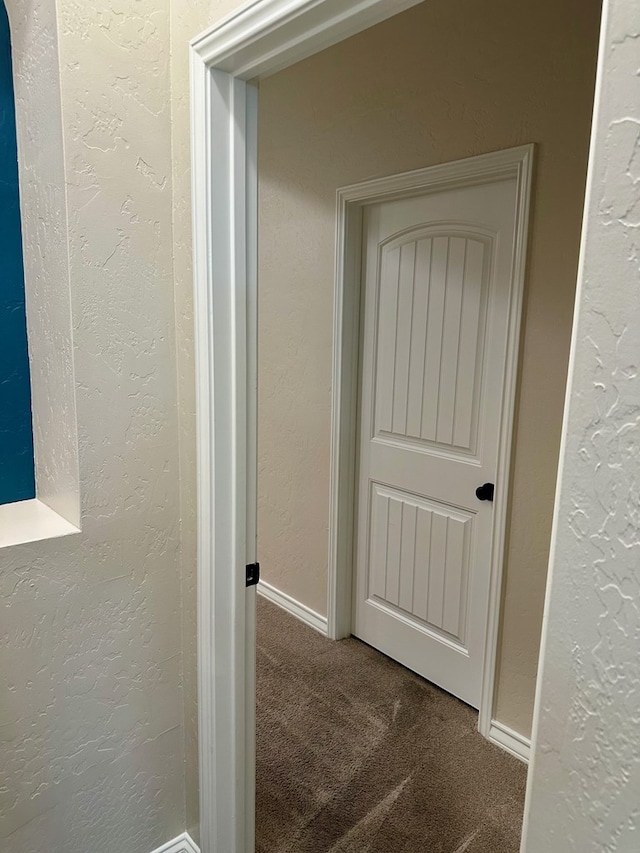 corridor featuring baseboards, a textured wall, and carpet floors