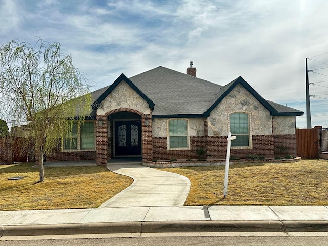 view of front facade with stone siding, fence, french doors, brick siding, and a chimney