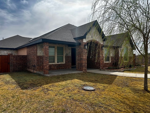 view of home's exterior featuring a patio, fence, a shingled roof, a lawn, and brick siding