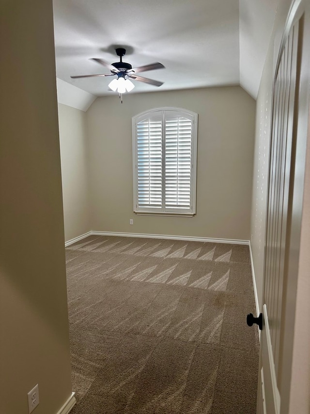 carpeted empty room with vaulted ceiling, a ceiling fan, and baseboards