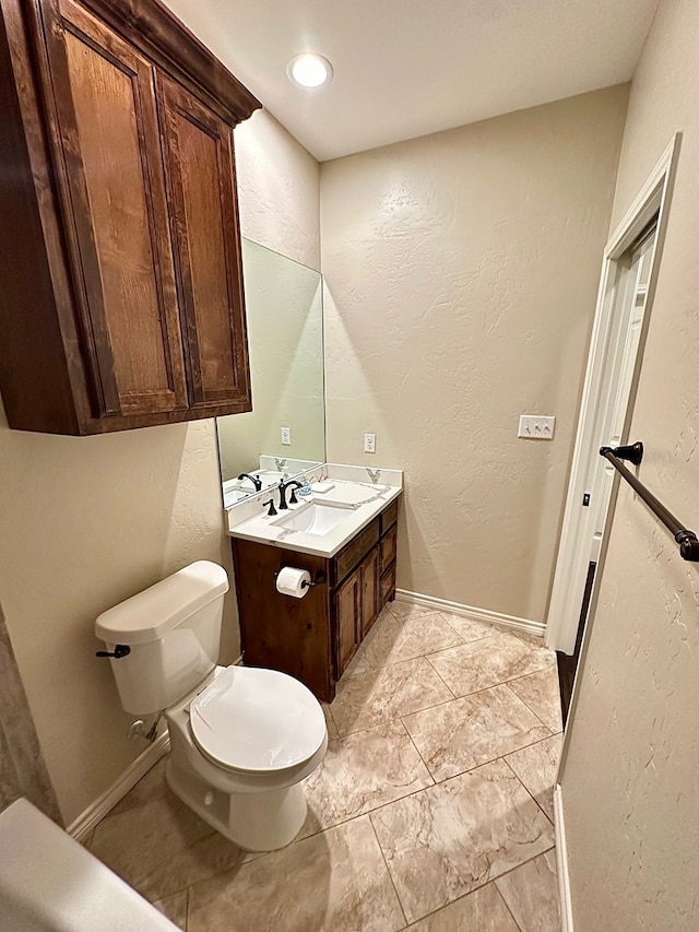 half bathroom with baseboards, toilet, vanity, and a textured wall