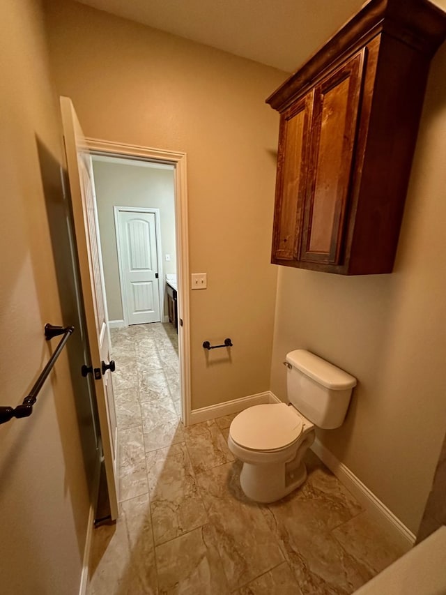 half bath with toilet, baseboards, and marble finish floor