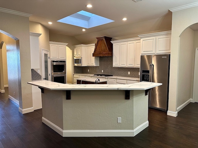 kitchen with arched walkways, appliances with stainless steel finishes, white cabinetry, and premium range hood