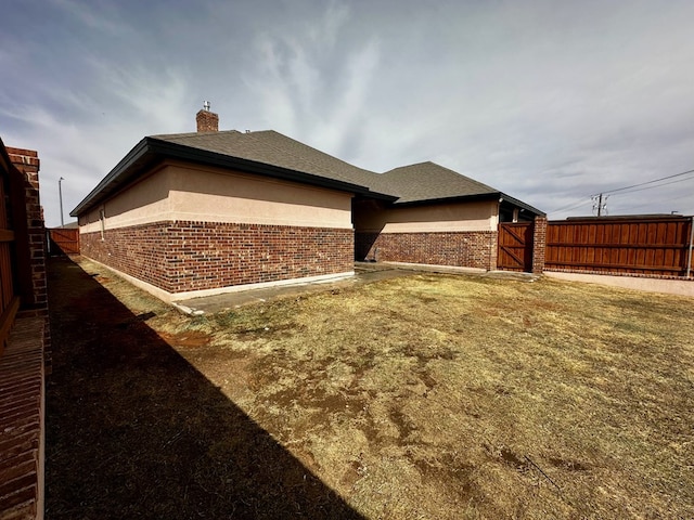 view of home's exterior featuring brick siding, a chimney, a gate, and fence