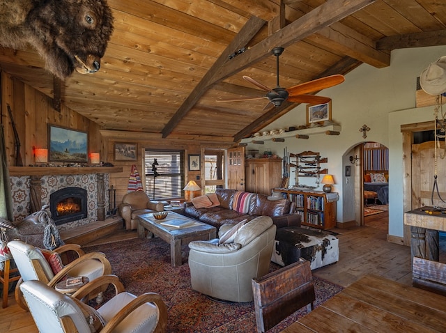 living room with a stone fireplace, wood walls, hardwood / wood-style floors, and lofted ceiling with beams