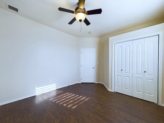 unfurnished bedroom featuring baseboards, visible vents, a ceiling fan, dark wood finished floors, and a closet