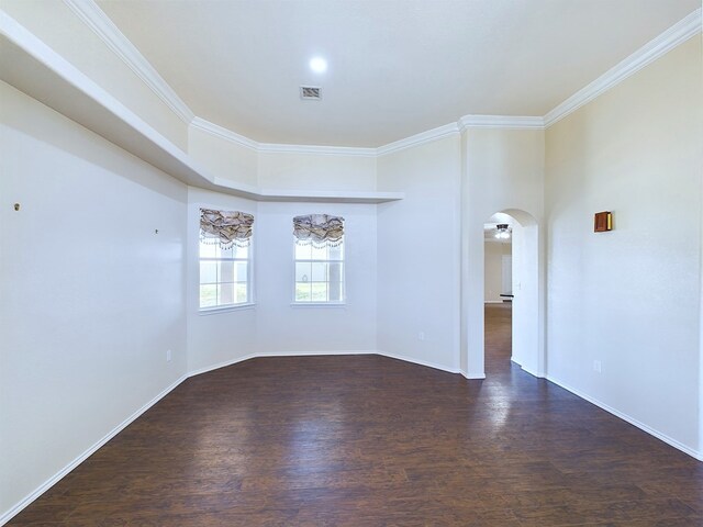 empty room featuring dark wood-style floors, visible vents, arched walkways, and ornamental molding