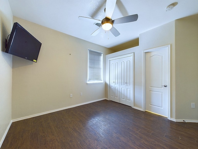 unfurnished bedroom featuring dark wood-style floors, a closet, baseboards, and a ceiling fan