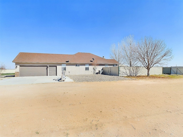 back of house with fence, driveway, an attached garage, and stucco siding