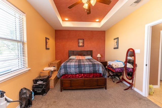 bedroom featuring light carpet, a tray ceiling, and ceiling fan