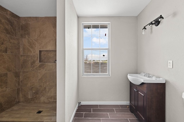 bathroom with tiled shower, vanity, and baseboards