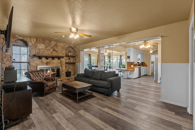 living room featuring a fireplace, ceiling fan, wood-type flooring, and a textured ceiling