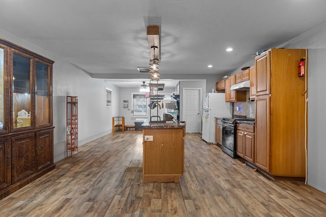 kitchen featuring wood finished floors, a center island with sink, stainless steel electric range, freestanding refrigerator, and under cabinet range hood