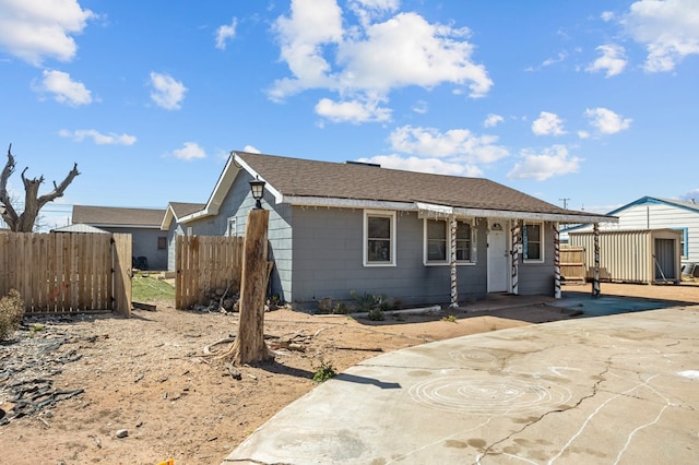 view of front of home with a shingled roof, concrete driveway, and fence