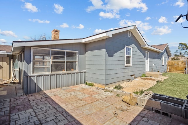 back of property featuring a chimney, a patio, and fence