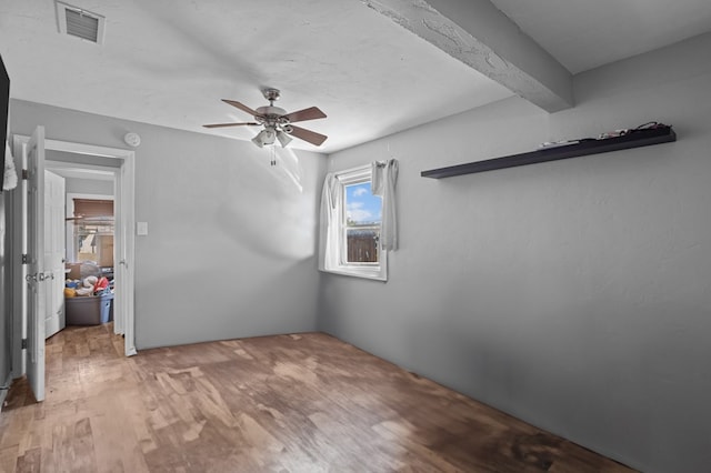 unfurnished bedroom featuring beam ceiling, visible vents, light wood-style flooring, and a ceiling fan