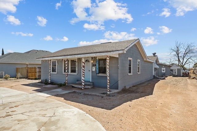 view of front facade featuring driveway, a shingled roof, and fence