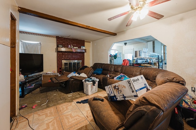 living room featuring ceiling fan, beam ceiling, and a brick fireplace