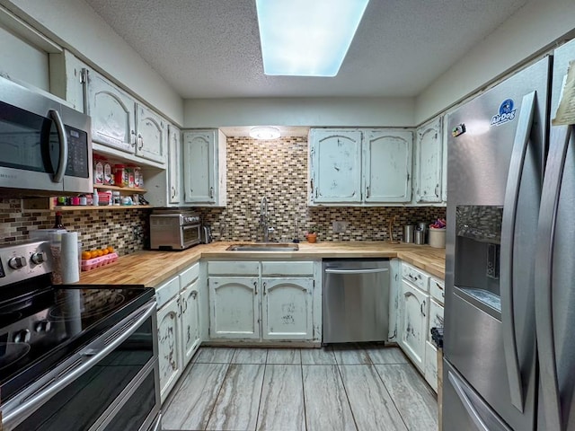 kitchen with backsplash, wooden counters, sink, a textured ceiling, and stainless steel appliances