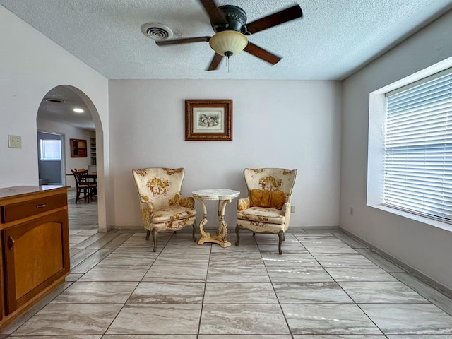 living area with ceiling fan, a healthy amount of sunlight, and a textured ceiling