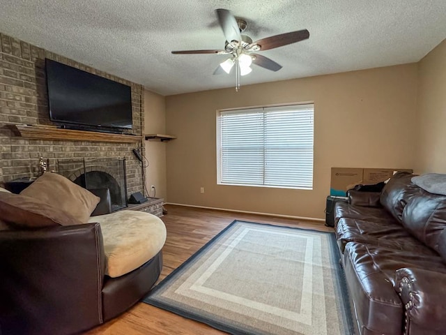 living room featuring ceiling fan, wood-type flooring, a textured ceiling, and a brick fireplace