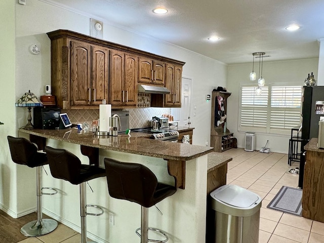 kitchen featuring dark stone counters, a kitchen breakfast bar, stainless steel range, tasteful backsplash, and decorative light fixtures