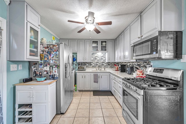 kitchen with sink, decorative backsplash, light tile patterned floors, stainless steel appliances, and a textured ceiling