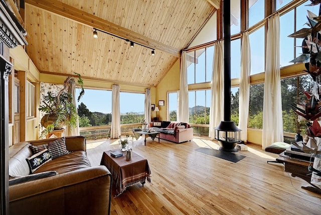 sunroom / solarium featuring lofted ceiling with beams, a wood stove, and wooden ceiling