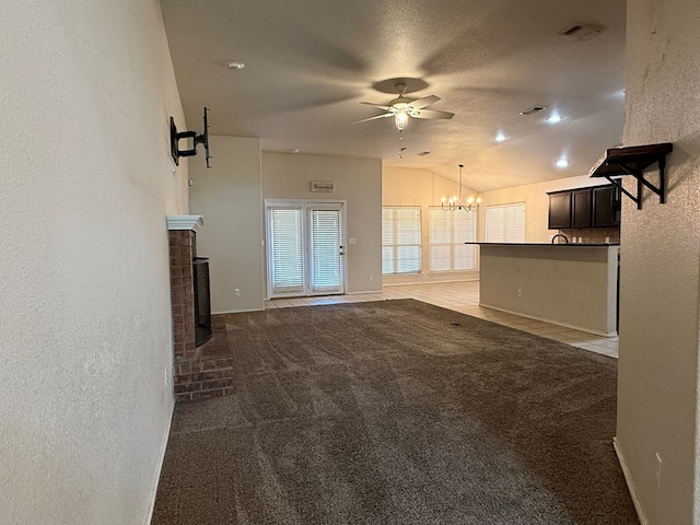 unfurnished living room with vaulted ceiling, ceiling fan with notable chandelier, carpet floors, and a brick fireplace