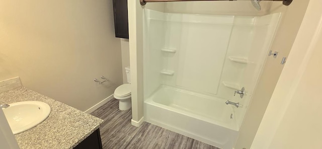 bathroom with baseboards, shower / washtub combination, toilet, wood finished floors, and vanity