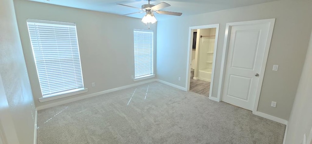 unfurnished bedroom featuring ceiling fan, baseboards, carpet flooring, multiple windows, and ensuite bathroom