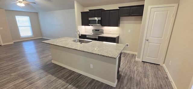 kitchen featuring dark cabinetry, an island with sink, dark wood-style flooring, a sink, and appliances with stainless steel finishes