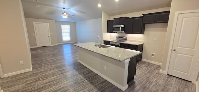 kitchen with dark wood-type flooring, a kitchen island with sink, a sink, dark cabinetry, and appliances with stainless steel finishes