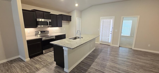 kitchen with a kitchen island with sink, dark wood-style flooring, a sink, vaulted ceiling, and appliances with stainless steel finishes