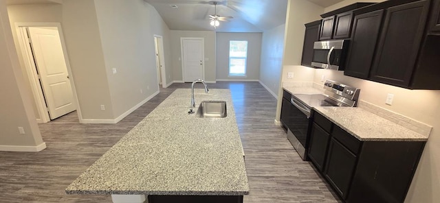 kitchen featuring dark wood finished floors, lofted ceiling, an island with sink, a sink, and stainless steel appliances