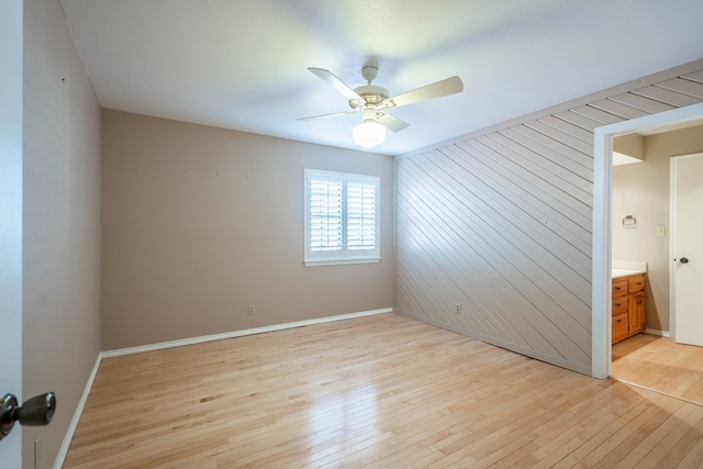 empty room featuring wood walls, ceiling fan, and light wood-type flooring