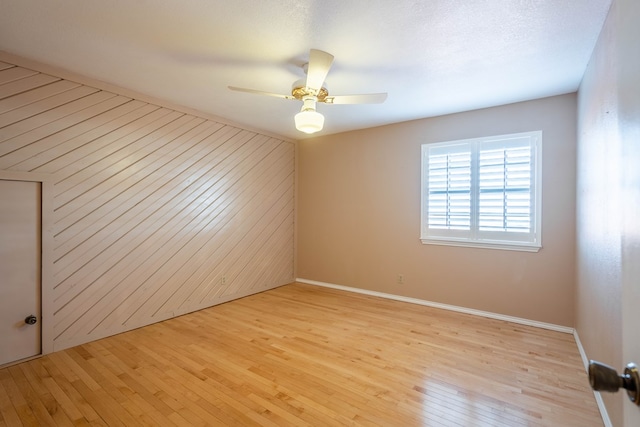 unfurnished room with light hardwood / wood-style floors, ceiling fan, and wood walls