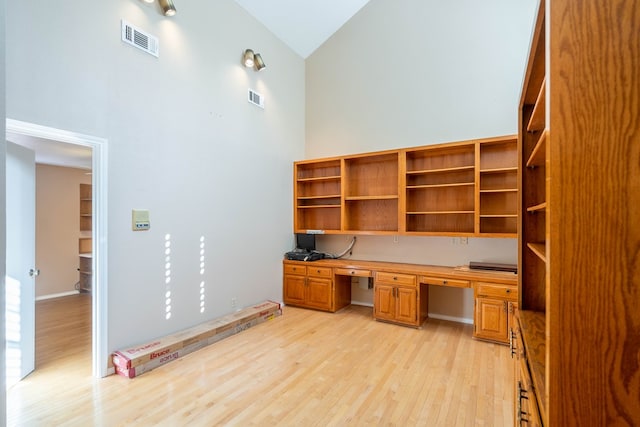 unfurnished office with built in desk, high vaulted ceiling, and light hardwood / wood-style flooring