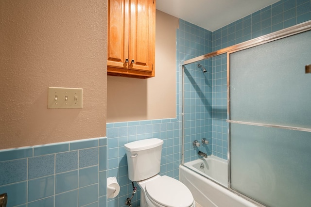 bathroom featuring toilet, combined bath / shower with glass door, and tile walls