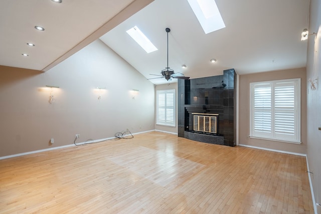 unfurnished living room with a skylight, high vaulted ceiling, light wood-type flooring, ceiling fan, and a tiled fireplace