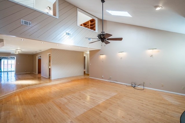 unfurnished living room featuring ceiling fan, high vaulted ceiling, a skylight, and light hardwood / wood-style floors