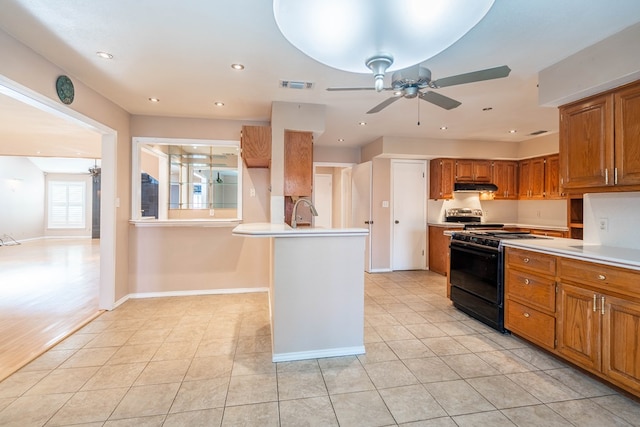 kitchen featuring an island with sink, light tile patterned floors, black range with gas stovetop, and ceiling fan