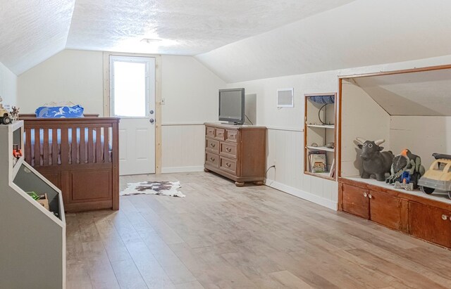 bonus room with a textured ceiling, light wood-type flooring, vaulted ceiling, and wood walls