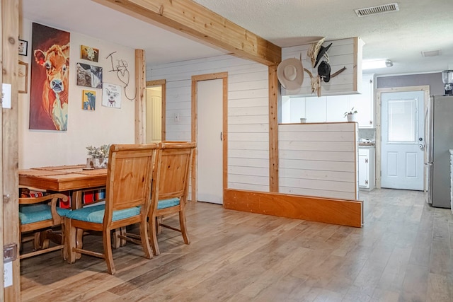 dining space featuring a textured ceiling, light hardwood / wood-style flooring, and wooden walls